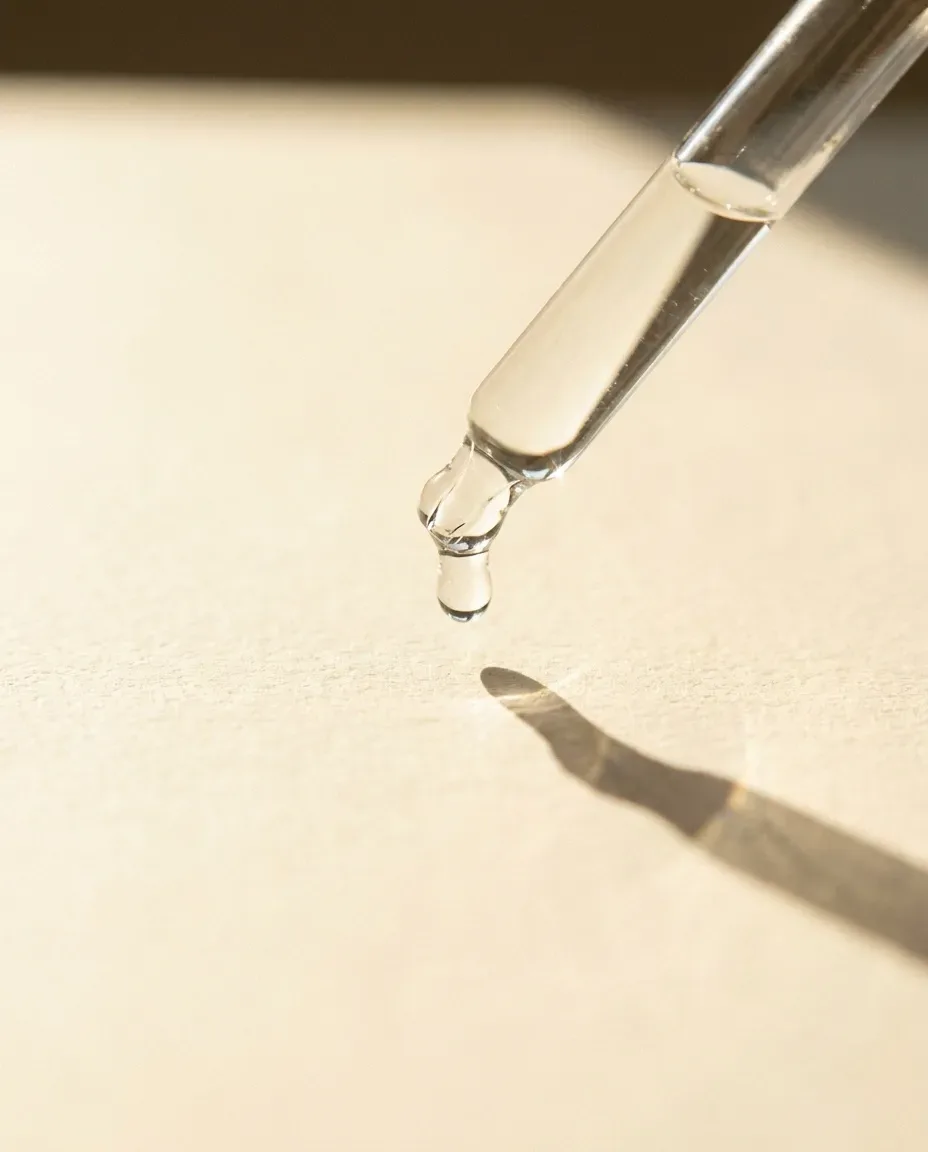 Glass dropper releasing a clear drop onto a pale surface