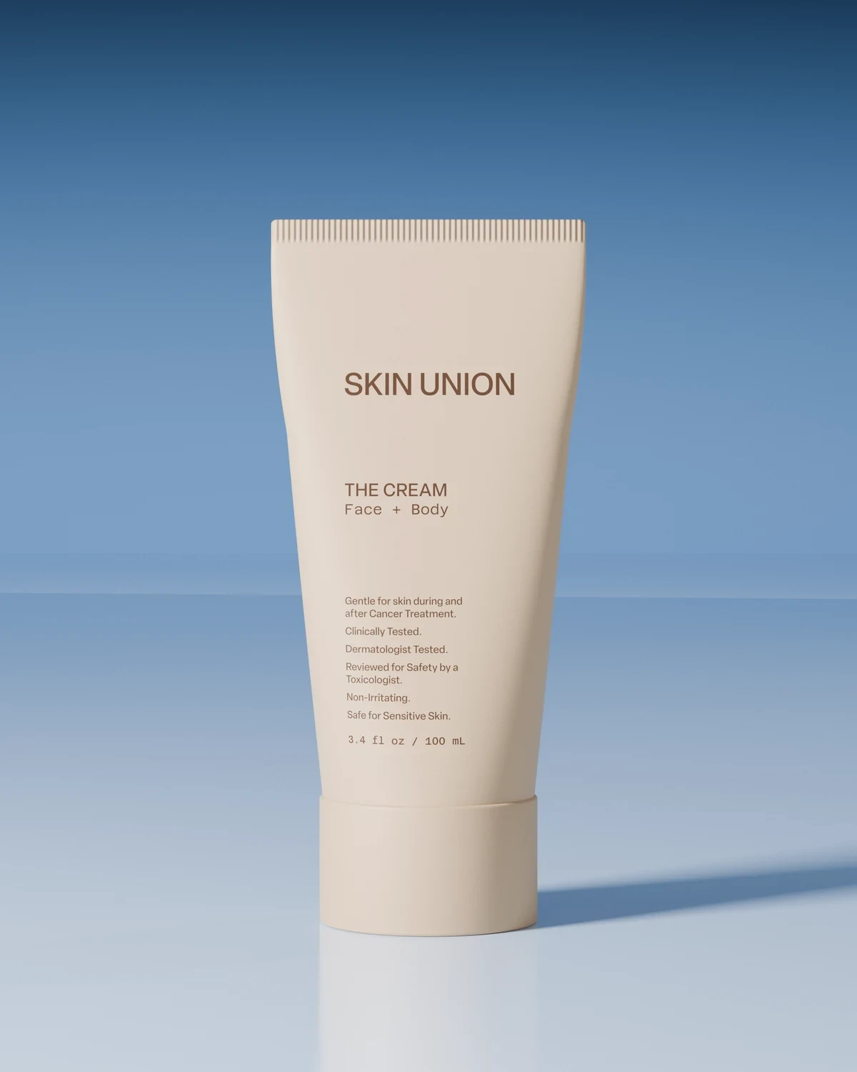 The Cream — a pale squeeze tube labelled Face + Body, standing upright on a soft white surface against a blue backdrop