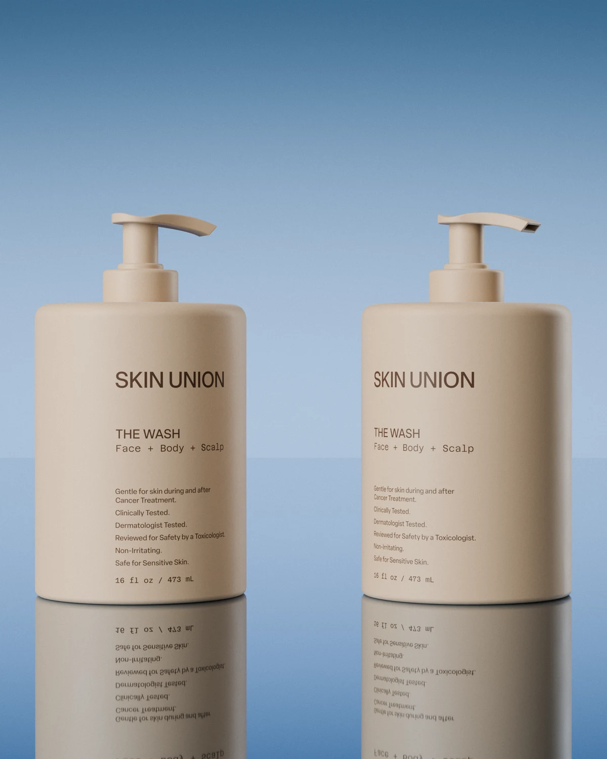 Two bottles of The Wash side by side, reflected on a glassy surface under a soft blue sky